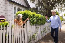Neighbors waving at each other outdoors over a fence