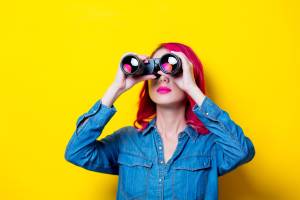 Woman with dyed hair holding binoculars to her eyes, looking up and away