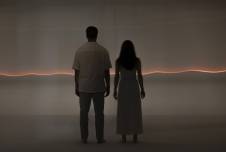 Couple seen from the back in gray landscape with a bright line around the horizon