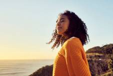 Woman standing on a cliff overlooking ocean with eyes closed peacefully
