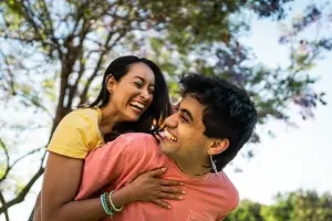 Couple piggybacking at the park smiling widely 