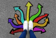 Looking down at legs and shoes with colorful arrows painted on the ground below them going in all directions