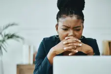 Woman frowning leaning on her hands looking down at laptop at work