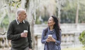 Couple walking and talking outdoors, holding coffees