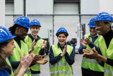Group of workers with helmets on standing in a circle smiling and clapping