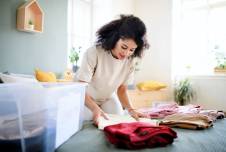 Woman folding clothes on her bed next to a box marked Charity 