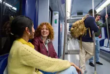 Two women talking on the subway with other passengers in the background