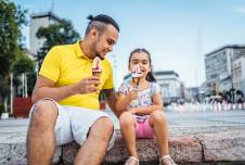 Father and daughter sitting on the sidewalk eating ice cream