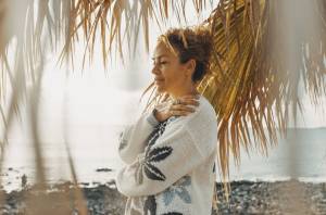 Woman on the beach with palm trees around her hugging herself