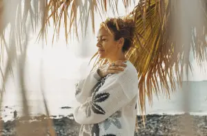 Woman on the beach with palm trees around her hugging herself