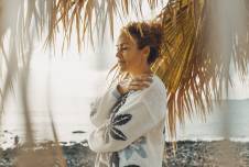 Woman on the beach with palm trees around her hugging herself