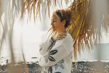 Woman on the beach with palm trees around her hugging herself