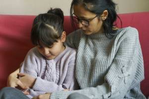 Mother with her arm around daughter, sitting on the couch together