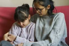 Mother with her arm around daughter, sitting on the couch together