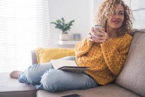 Woman sitting on her couch with a hot beverage and her notebook open in front of her