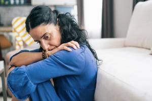 Woman sitting by her couch with head on her crossed arms, thinking