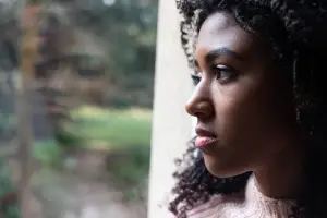 A young woman stares out her window into the distance in contemplation.