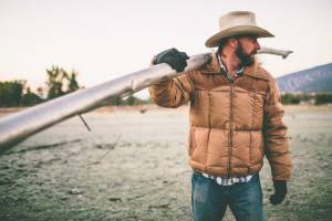 Man standing in field carrying irrigation pipe over his shoulder