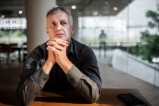 Man sitting at a table clasping his hands looking up and thinking