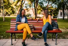 Two friends sit on a park bench talking