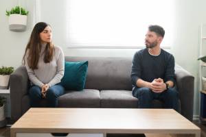 Couple sitting on opposite ends of a couch looking at each other with serious expressions