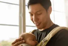 Dad smiling holding a baby in a sling