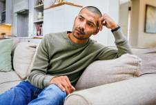 Man sitting on couch looking troubled, hand on head