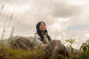 Woman sitting in nature with her eyes closed peacefully