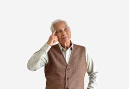 An image showing an elderly man in a vest, thoughtfully touching his temple