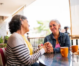 Women sitting at a cafe smiling at each other and clasping hands