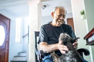 Old man sitting in a chair smiling down at a dog who has its paws in his lap