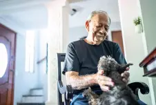 Old man sitting in a chair smiling down at a dog who has its paws in his lap