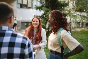 Three college students standing outside on campus talking and smiling
