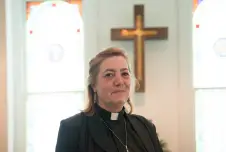 A priest smiling in front of a cross