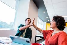 Two coworkers sitting at a desk doing a high five