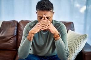 Stressed man sitting on the couch, with his head in his hands