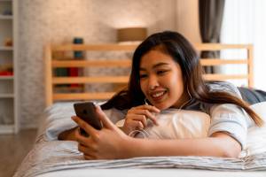 An image of a teenage girl lying on her bed, smiling while looking at her phone, suggesting that screen time during the pandemic might have positive aspects for teens.