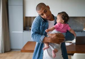 Father holding baby and holding phone between his ear and shoulder