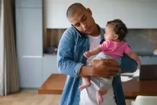 Father holding baby and holding phone between his ear and shoulder