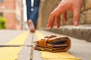 A close-up image of a hand reaching down to pick up a wallet lying on a yellow line on the street