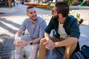 Two friends sitting on a bench talking with a drink
