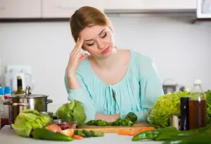 a picture of a woman sitting in front of a table full of vegetables, looking bored of them