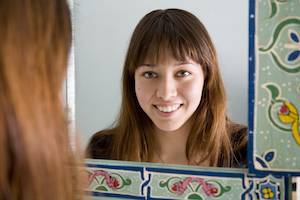 A woman with long hair is smiling at her reflection in a decorative mirror