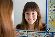 A woman with curly hair wearing a red shirt looks at herself in a mirror