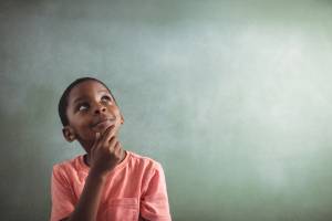 An image showing a young student thinking, with a thoughtful expression, set against a green chalkboard background