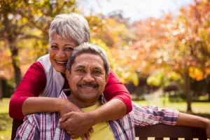 An image showing an elderly couple embracing and smiling in an outdoor setting with autumn foliage