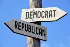 an image showing two directional signs on a wooden pole pointing in opposite directions, labeled "DEMOCRAT" and "REPUBLICAN