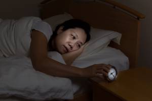 a person in bed, looking worried while holding an alarm clock